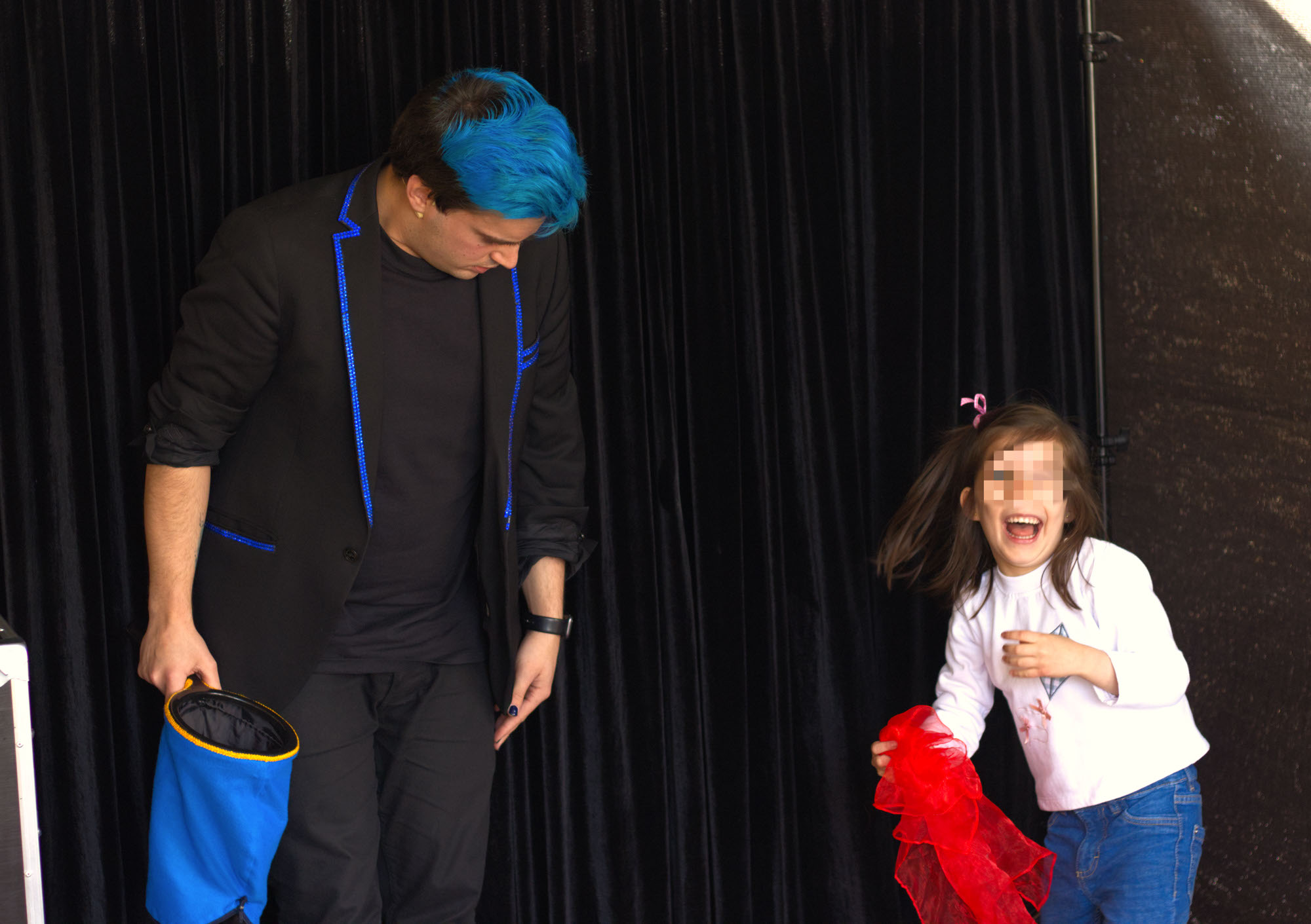 Niña sujetando un pañuelo rojo mientras se ríe y el mago cumple Ivan Torres sujeta la bolsa azul