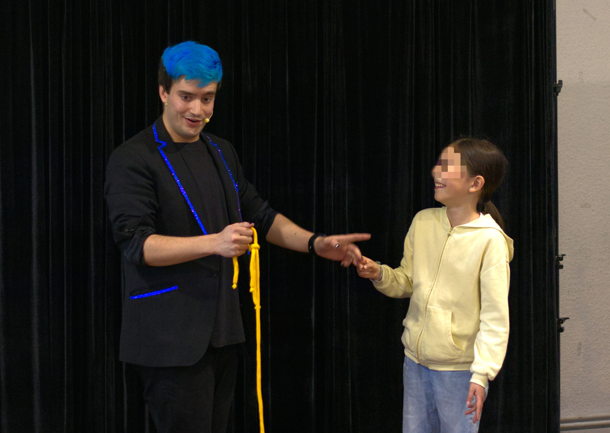 Mago Ivan Torres con una cuerda en la mano mientras señala a la niña que sonríe a su lado